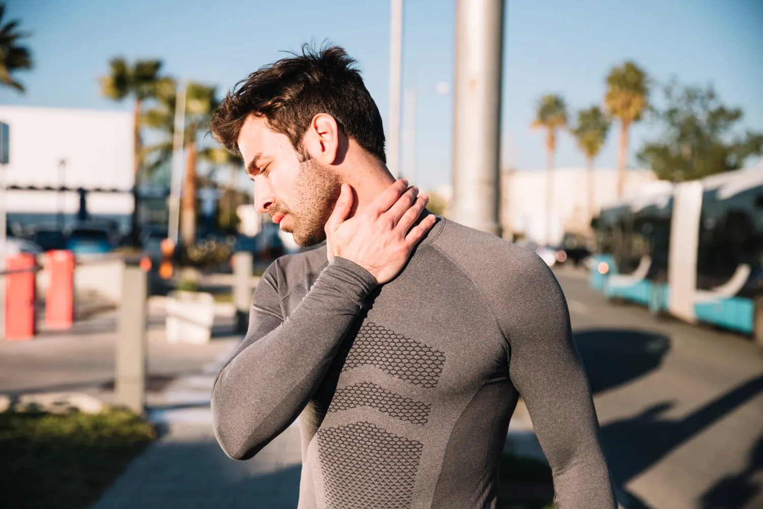 Athletic man outdoors holding neck in pain, possibly from chronic pain or tension