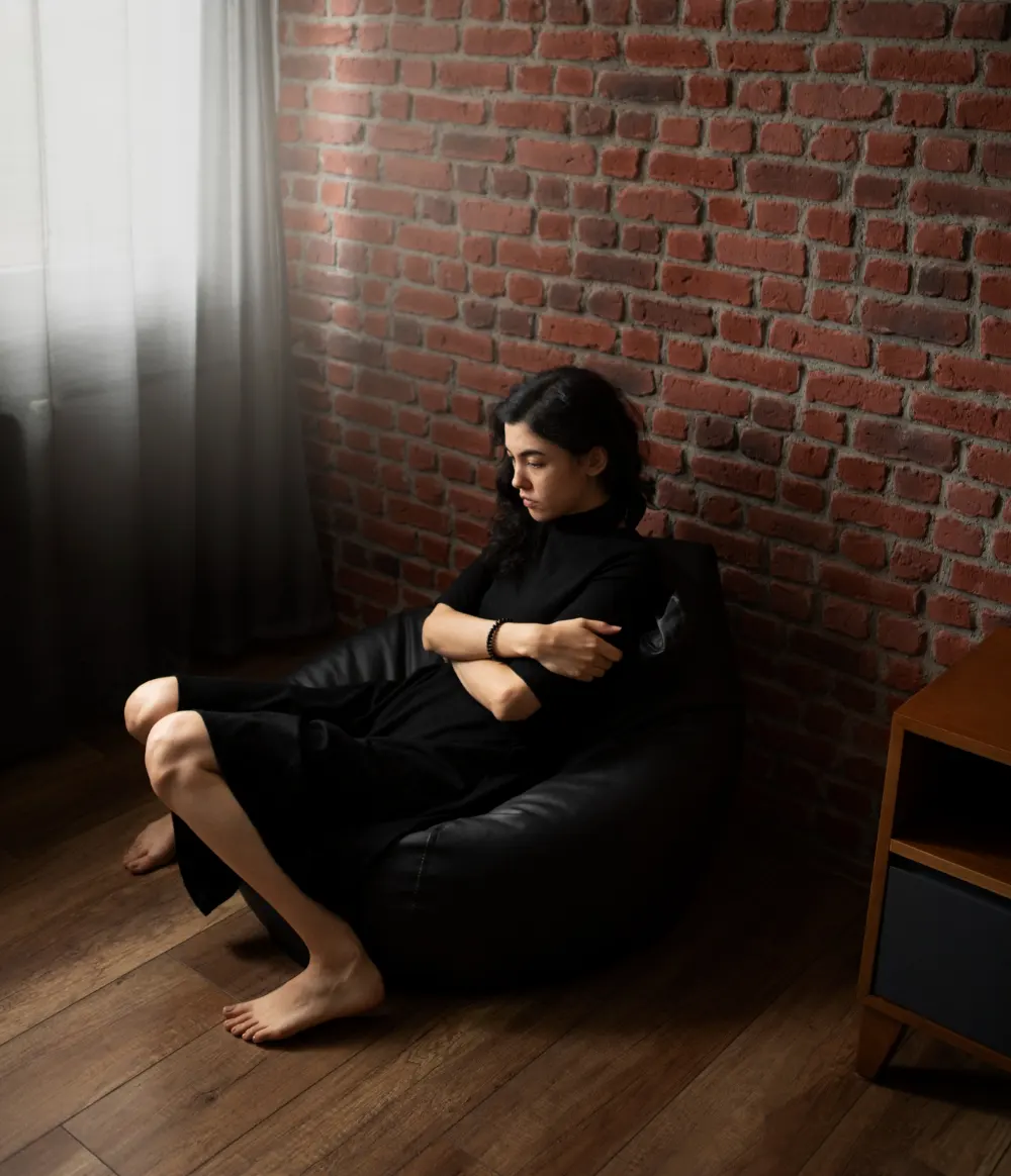 Woman sitting alone in a dark room on a beanbag, appearing withdrawn and depressed