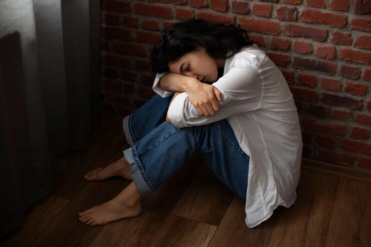 Young woman curled up on the floor against a brick wall, showing signs of PTSD and emotional distress