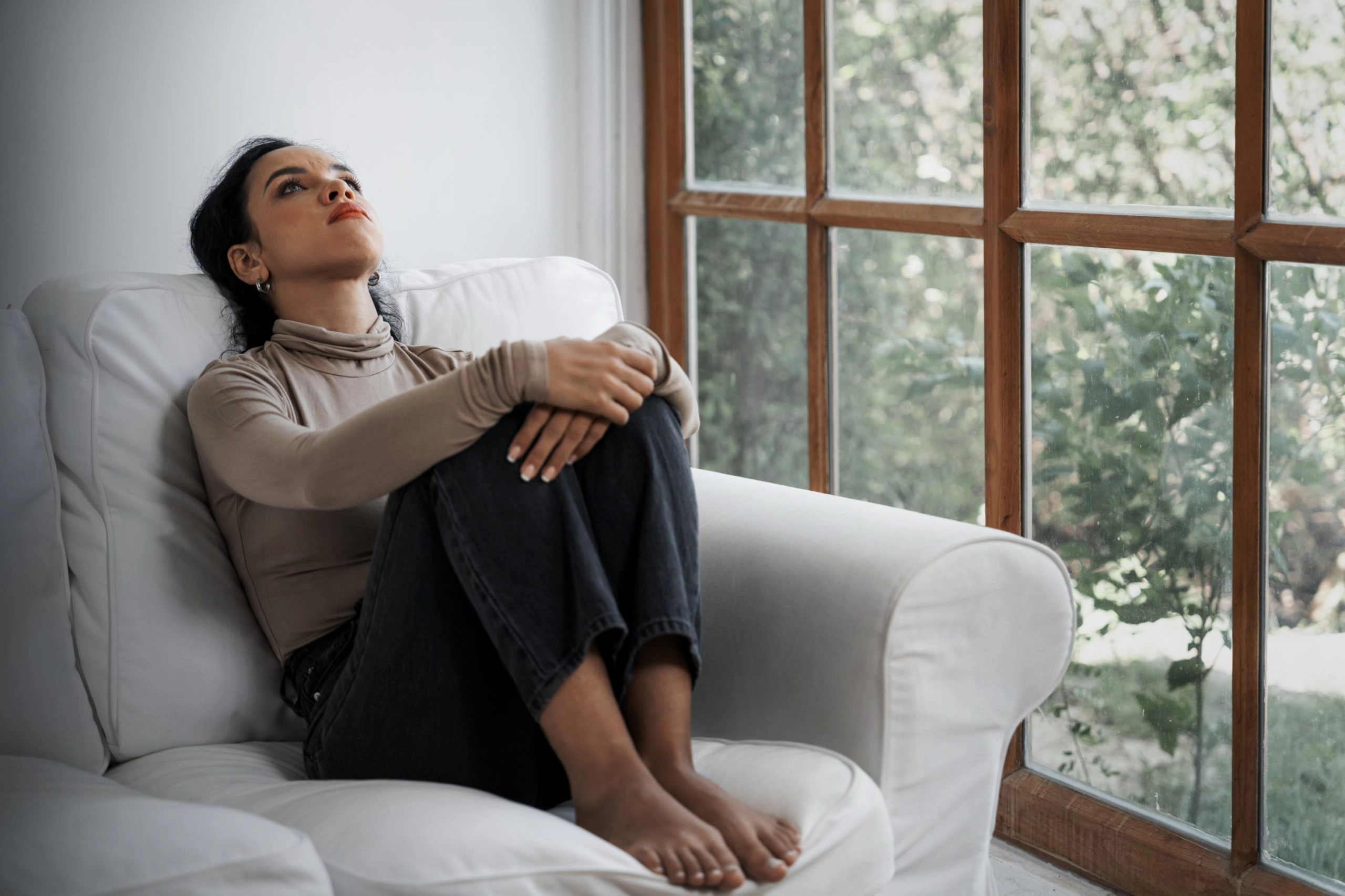 person sitting on couch next to the window struggling with anxiety
