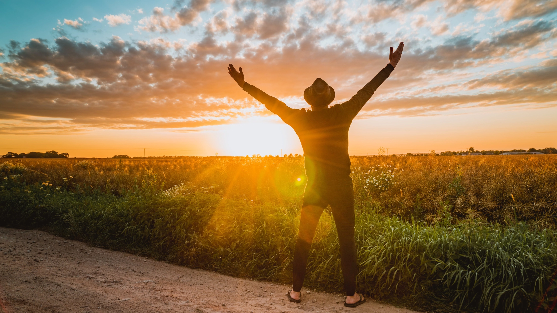 person with their hands raised as the sun is rising