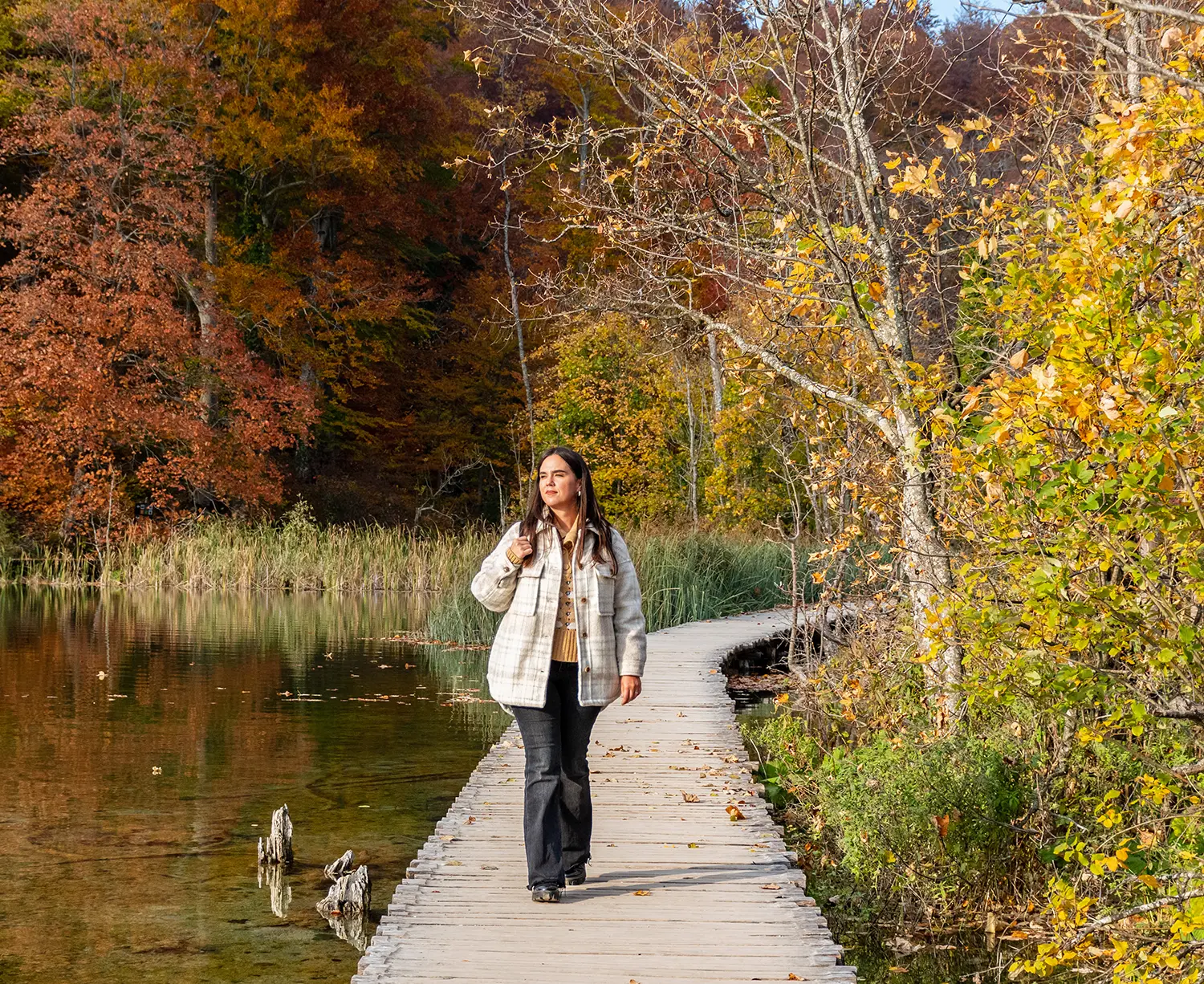 Woman walking alone in nature along a boardwalk during fall, representing mental clarity and healing journey