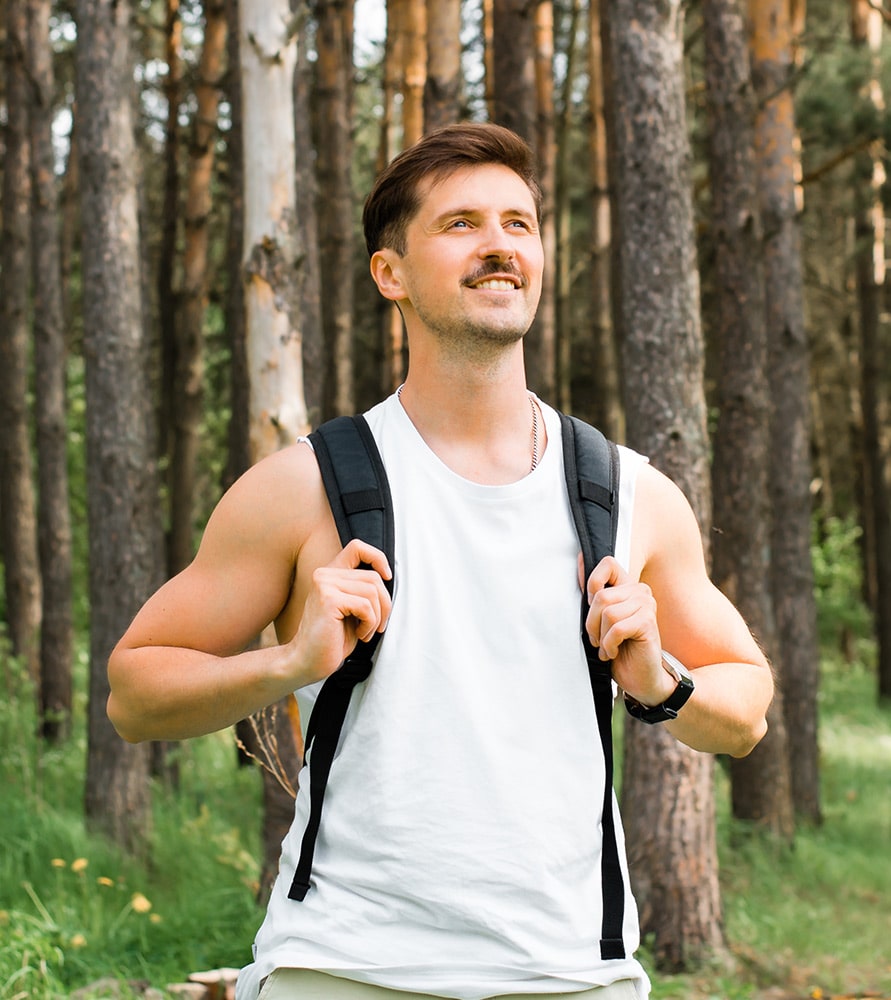 Smiling man hiking through the forest with a backpack, representing improved mental clarity and emotional well-being after treatment