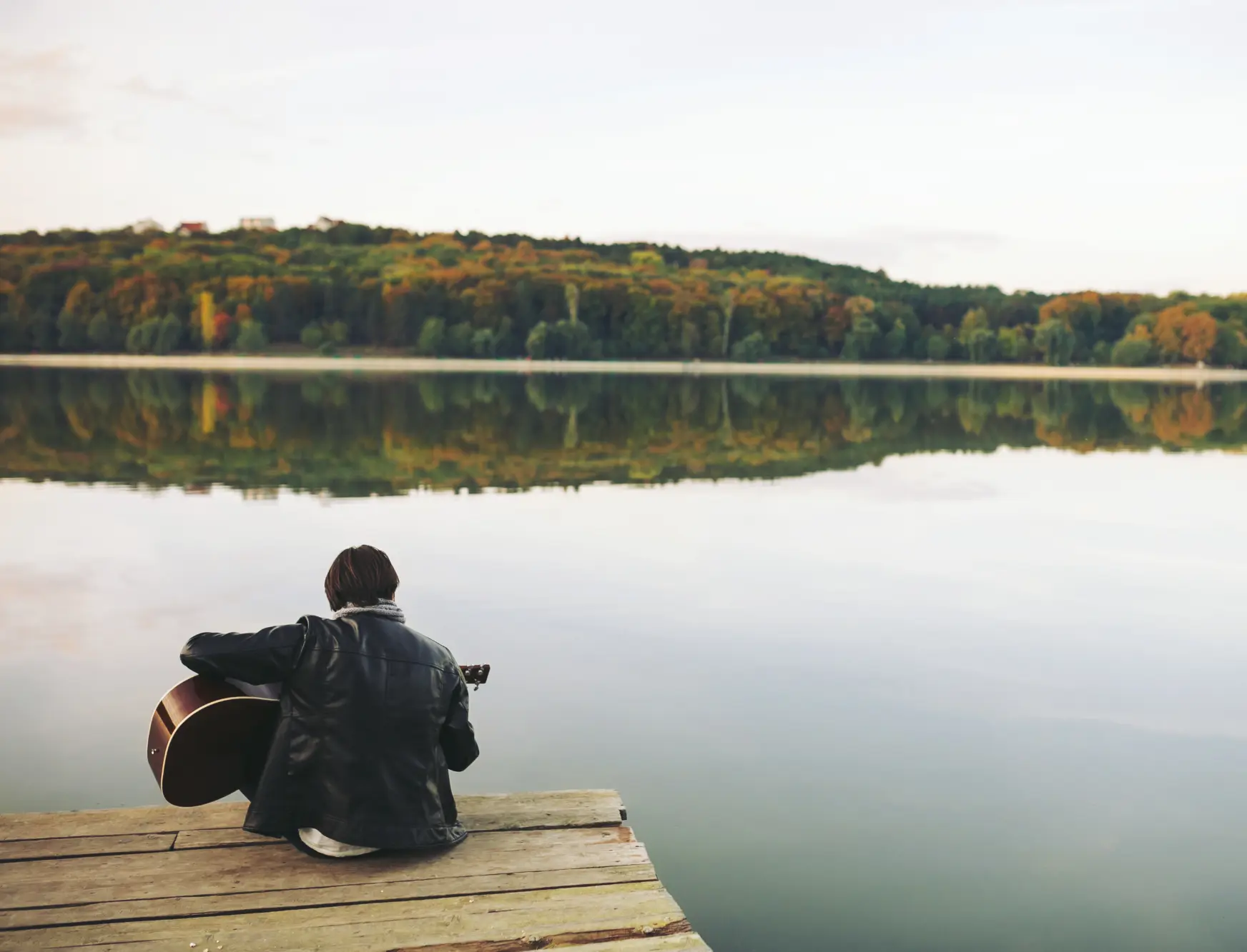 person sitting on the pier next to a calm lake